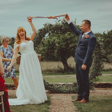 Katie and Mitch hold up their handfasting ribbons
